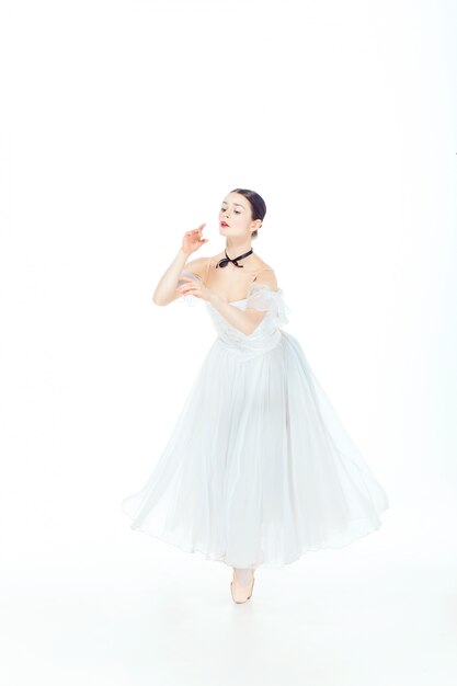 Bailarina en vestido blanco posando en zapatillas de punta, estudio.