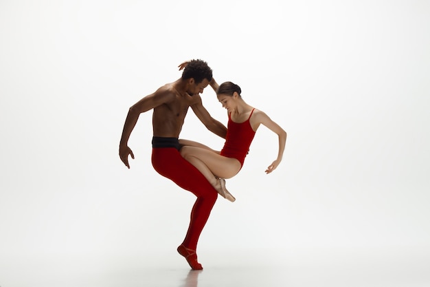 Bailarines de ballet clásico agraciado bailando aislado sobre fondo blanco de estudio. Pareja con ropa de color rojo brillante como una combinación de vino y leche. El concepto de gracia, artista, movimiento, acción y movimiento.