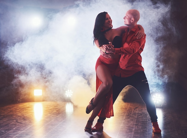 Bailarines expertos actuando en el cuarto oscuro bajo la luz del concierto y el humo. Sensual pareja realizando una danza contemporánea artística y emocional