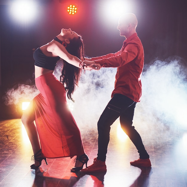 Bailarines expertos actuando en el cuarto oscuro bajo la luz del concierto y el humo. Sensual pareja realizando una danza contemporánea artística y emocional
