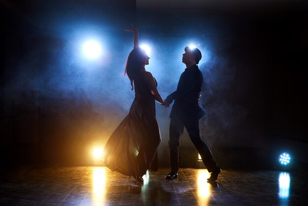 Bailarines expertos actuando en el cuarto oscuro bajo la luz del concierto y el humo. Sensual pareja realizando una danza contemporánea artística y emocional