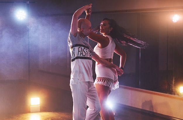 Foto gratuita bailarines expertos actuando en el cuarto oscuro bajo la luz del concierto y el humo. sensual pareja realizando una danza contemporánea artística y emocional