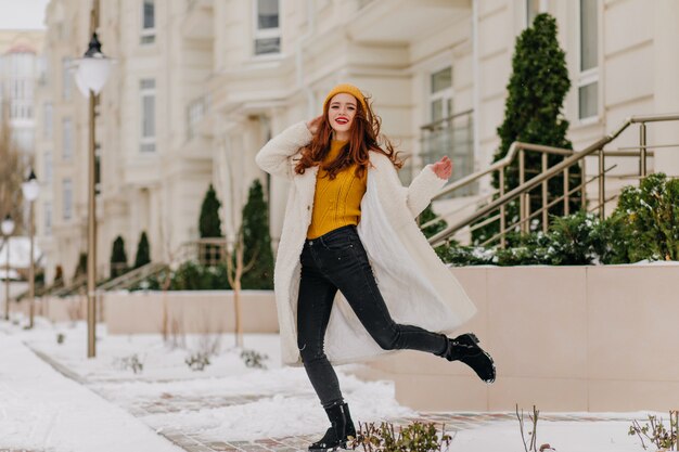Baile divertido de la muchacha despreocupada en día de invierno. Foto al aire libre de la encantadora dama de jengibre en bata blanca.
