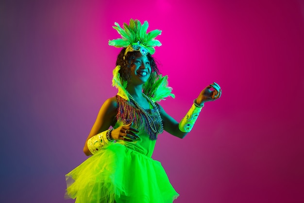 Foto gratuita baile. hermosa mujer joven en carnaval, elegante disfraz de mascarada con plumas bailando en la pared degradada en neón. concepto de celebración navideña, tiempo festivo, baile, fiesta, diversión.