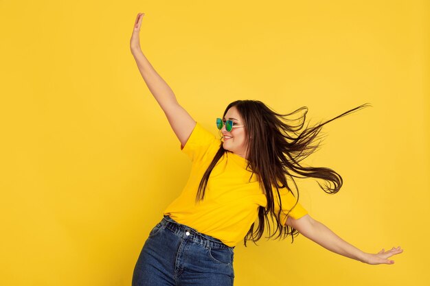 Baile inspirado en gafas de sol. Mujer caucásica en pared amarilla. Modelo morena mujer hermosa en estilo casual. Concepto de emociones humanas, expresión facial, ventas, anuncios, copyspace.