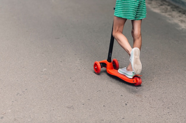 Foto gratuita baja sección de una niña montando scooter en carretera