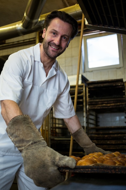 Foto gratuita baker, manteniendo la bandeja de bollos horneados en estantería