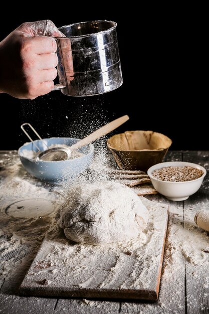 Baker tamizar harina a través de un tamiz en la mesa de madera