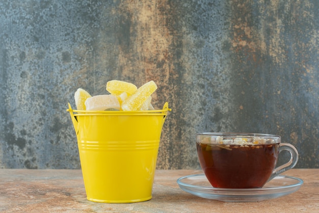 Foto gratuita un balde amarillo lleno de caramelos de gelatina de azúcar y una taza de té de hierbas