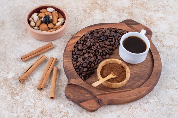 Bandeja de café junto a palitos de canela y un tazón pequeño de frutos secos variados