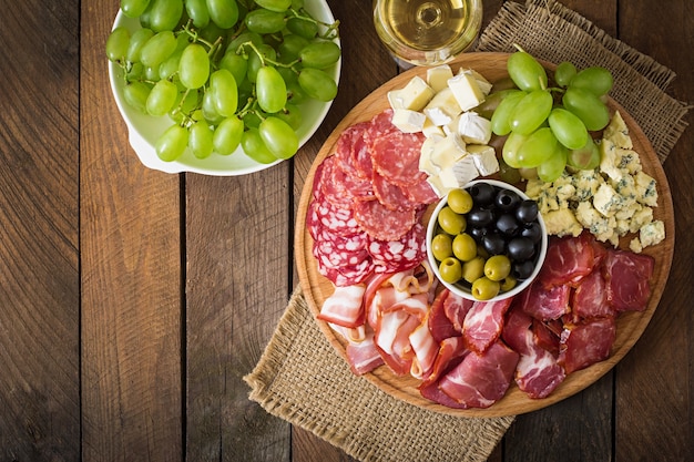 Bandeja de catering antipasto con tocino, cecina, salami, queso y uvas en una mesa de madera