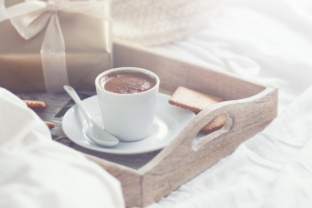 Bandeja de desayuno con un café, galletas y un regalo dorado