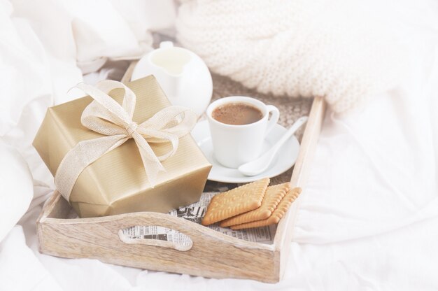 Bandeja de desayuno con un café, galletas y un regalo dorado