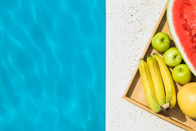 Bandeja con frutas colocadas en el borde de la piscina.