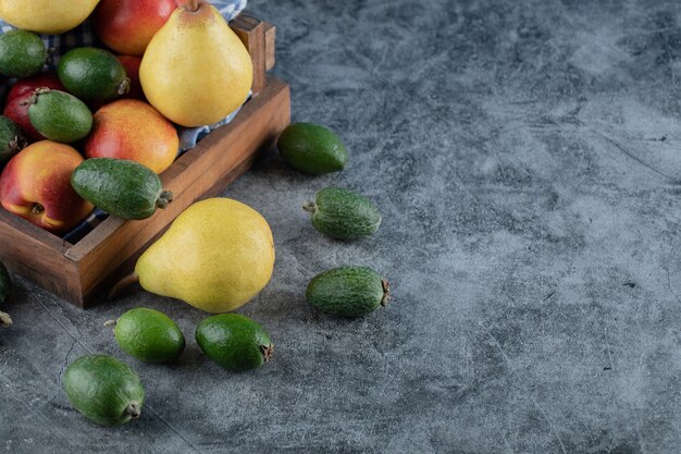 Foto gratuita una bandeja de frutas de madera llena de peras, feijoas y melocotones.