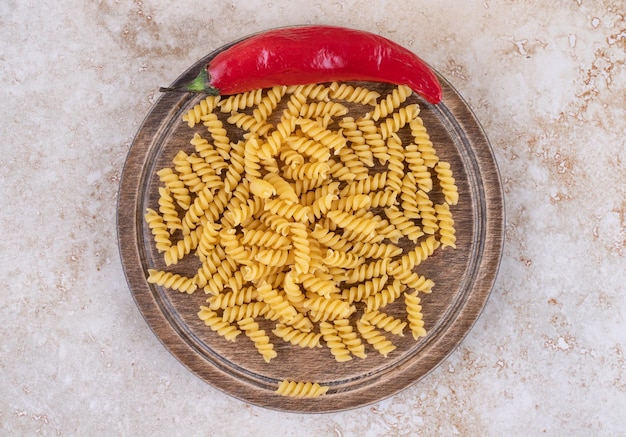 Bandeja de madera pequeña de pasta cruda con ají sobre superficie de mármol.