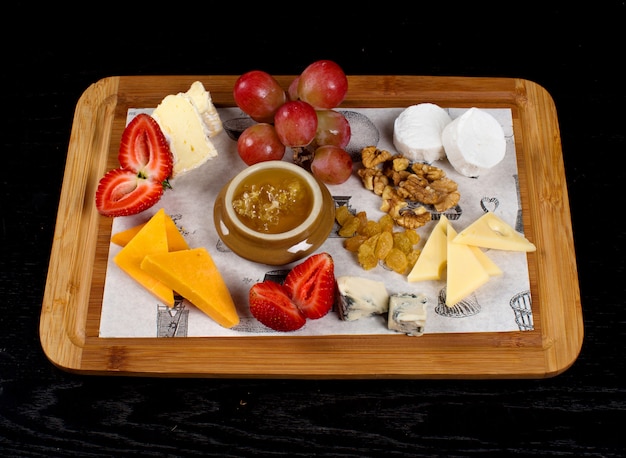 Foto gratuita bandeja de madera con quesos, frutas y un tarro de miel.