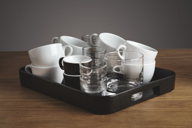Bandeja negra de plástico con café blanco limpio, té, vasos y tazas de whisky. en la mesa de madera gruesa en la cafetería. Aislado sobre fondo gris.