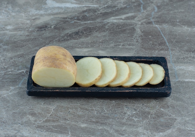 Una bandeja de patatas en rodajas, sobre la mesa de mármol.