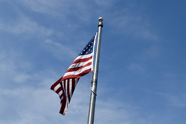 Bandera americana cerca de árboles bajo un cielo nublado azul y la luz solar