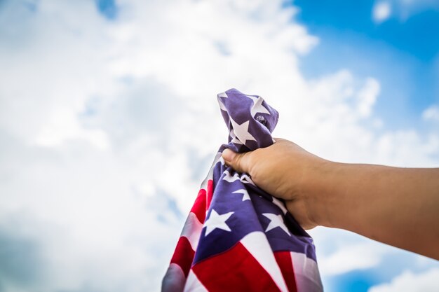 Bandera americana sujetada por una mano con nubes de fondo