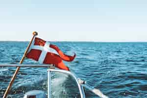 Foto gratuita y bandera blanca en un barco flotando sobre el océano bajo un cielo azul durante el día