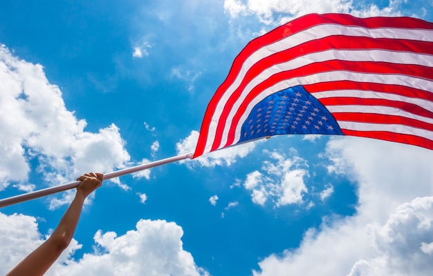 Bandera de Estados Unidos con estrellas y rayas sostener con las manos contra blu