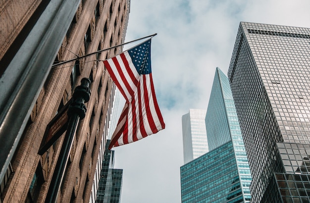 La bandera de Estados Unidos o Estados Unidos de América en un asta de bandera cerca de rascacielos bajo un cielo nublado