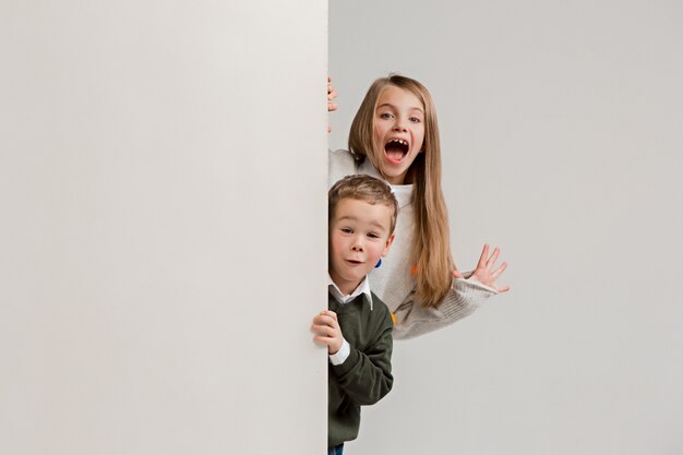 Banner con niños sorprendidos que miran a escondidas en el borde con copyspace. Retrato de lindo niño y niñas de niños pequeños mirando a la cámara contra la pared blanca del estudio.