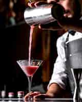Foto gratuita bar tierna vierte un cóctel de una coctelera en una copa de martini