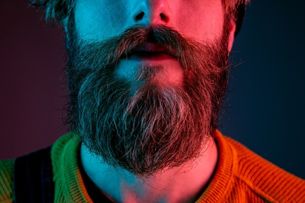 Barba bien cuidada, piel, de cerca. Retrato de hombre caucásico sobre fondo de estudio degradado en luz de neón. Hermoso modelo masculino con estilo hipster. Concepto de emociones humanas, expresión facial, ventas, publicidad.