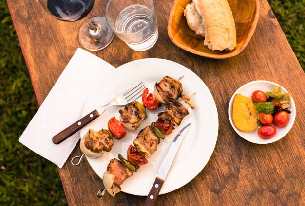 Barbacoa de carnes y verduras en mesa y copa de vino.