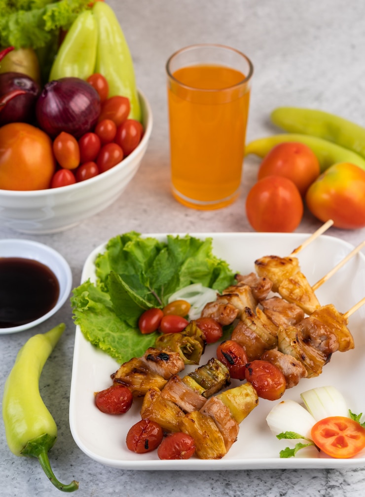 Foto gratuito barbacoa con una variedad de carnes, completa con tomates y pimientos en un plato blanco.
