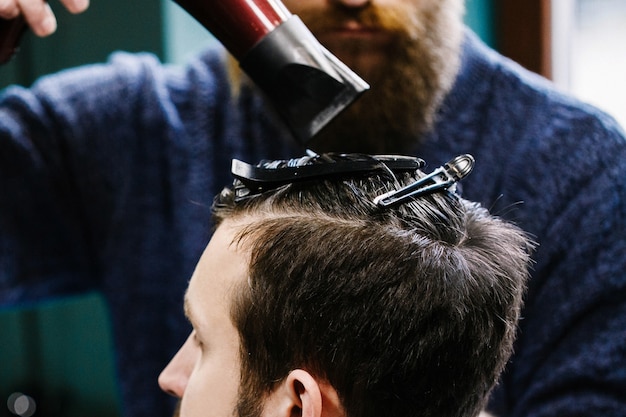 Barber utiliza un secador de pelo mientras secciona el cabello del hombre