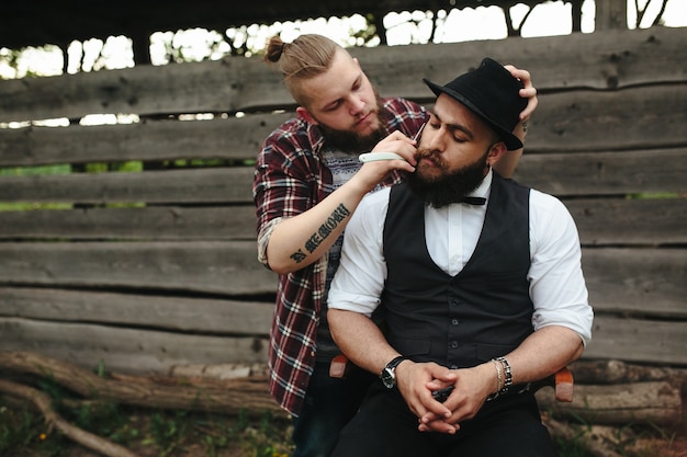 Foto gratuita barbero afeita a un hombre barbudo en ambiente vintage