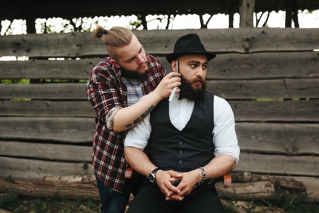 Foto gratuita barbero afeita a un hombre barbudo en ambiente vintage