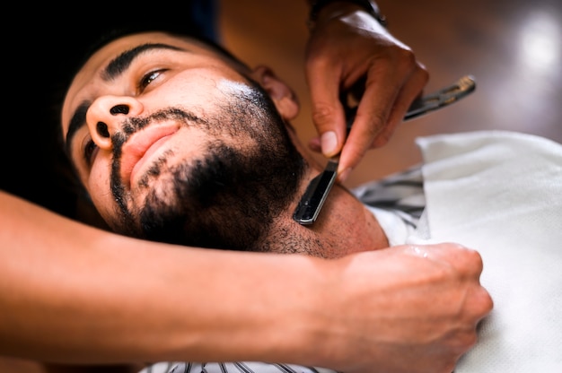 Barbero de alto ángulo afeitado la barba del hombre