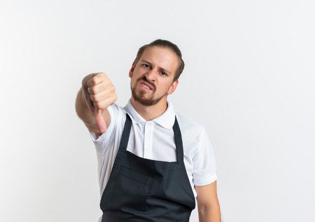 Barbero guapo joven disgustado vistiendo uniforme mostrando el pulgar hacia abajo aislado sobre fondo blanco con espacio de copia