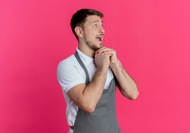 barbero hombre en delantal tomados de la mano juntos feliz y emocionado mirando a un lado de pie sobre la pared rosa