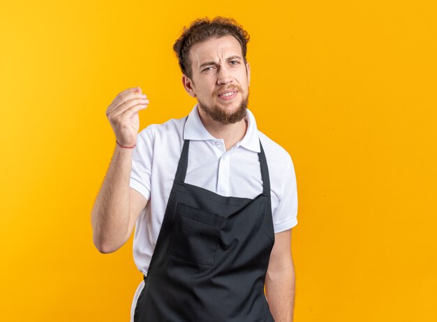 Barbero masculino joven disgustado vistiendo uniforme mostrando gesto de punta aislado sobre fondo amarillo