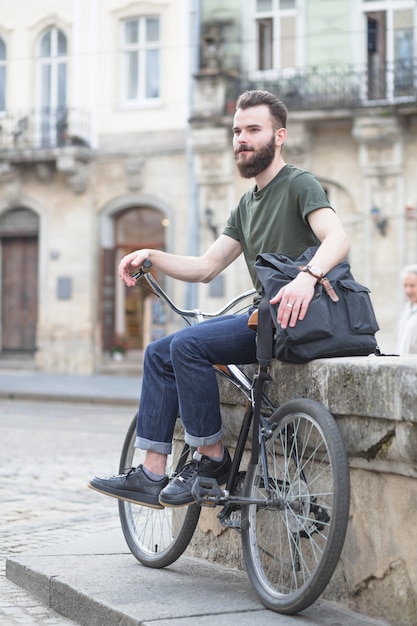 Barbudo joven sentado con su bicicleta en la ciudad