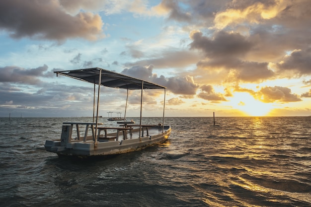 Barco artesanal de madera en el mar bajo un cielo nublado y la luz del sol durante la puesta de sol