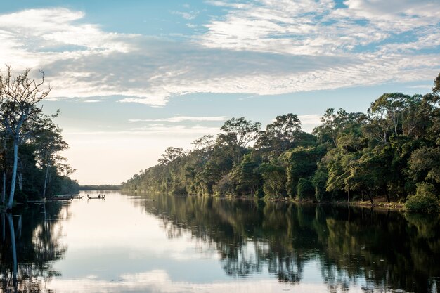 Barco, bosque, río y cielo azul en reflexión.