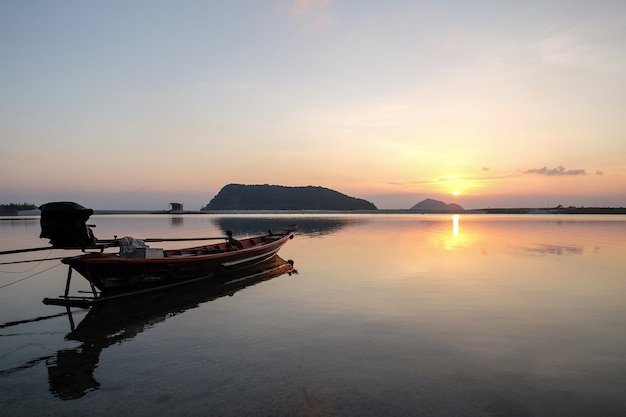 Barco en el mar rodeado de colinas con el sol reflejándose en el agua durante la puesta de sol