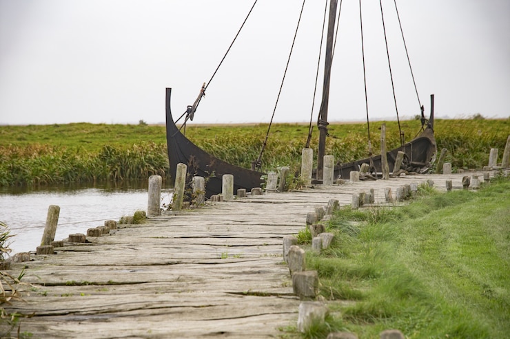 Foto gratuito barco oxidado en el lago cerca del muelle de madera en un pueblo vikingo bajo el cielo despejado