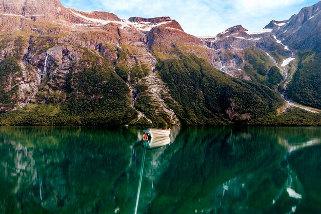 Barco de pesca en un lago inmóvil con altas montañas en fondo