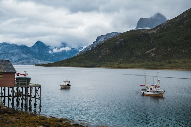 barcos de pesca navegando en el lago cerca de las montañas bajo el cielo nublado