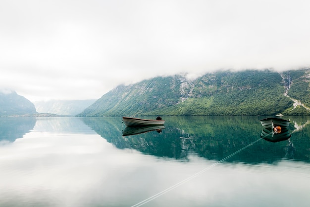 Barcos solitarios en un lago tranquilo con montaña brumosa en el fondo
