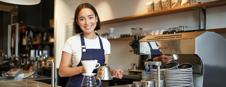Foto gratuito barista asiática sonriente vertiendo agua de la tetera filtrando café en el café de atrás