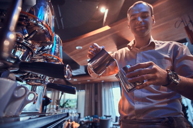 El barista enfocado está preparando café para los clientes usando una nueva y brillante cafetera.